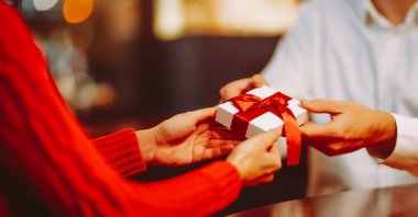 Hediye değişimi. Adam kadınına kırmızı kurdeleli bir hediye kutusu veriyor. Romantik bir gün..