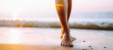 Yakın plan, genç bir kadın yaz sahilinde deniz suyu ve kum dalgası boyunca yürüyor..