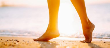 Yakın plan, genç bir kadın yaz sahilinde deniz suyu ve kum dalgası boyunca yürüyor..