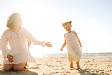 Mutlu anne ve kız güneşli bir günde sahilde eğleniyorlar. Güzel bir kadın ve kız birlikte vakit geçiriyorlar, dışarıda vakit geçiriyorlar. Çocukluk ve annelik kavramları.