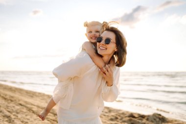 Mutlu anne ve kız güneşli bir günde sahilde eğleniyorlar. Güzel bir kadın ve kız birlikte vakit geçiriyorlar, dışarıda vakit geçiriyorlar. Çocukluk ve annelik kavramları.