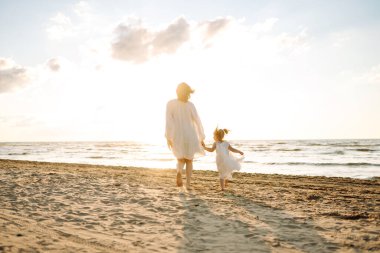 Mutlu anne ve kız güneşli bir günde sahilde eğleniyorlar. Güzel bir kadın ve kız birlikte vakit geçiriyorlar, dışarıda vakit geçiriyorlar. Çocukluk ve annelik kavramları.