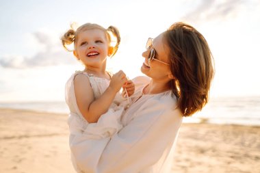 Mutlu anne ve kız güneşli bir günde sahilde eğleniyorlar. Güzel bir kadın ve kız birlikte vakit geçiriyorlar, dışarıda vakit geçiriyorlar. Çocukluk ve annelik kavramları.