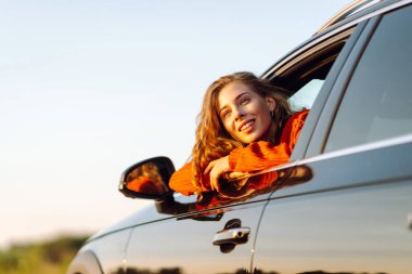 Araba penceresinden ya da çatısından sarkan bir kadın gezgin gün batımının özgürlüğünü hisseder. Yolculukta olan bir kadın güneşli bir günün tadını çıkarır. Macera konsepti, kırsal alan. Yaşam biçimi.