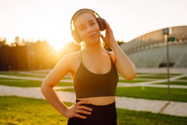 Atletik kadın koşudan ya da antrenmandan önce ısınıyor, güneş altında kablosuz kulaklık takıyor. Spor giyim sektöründeki kadınlar güneşli bir günün tadını çıkarıyorlar, müzik dinliyor ve egzersiz yapıyorlar. Spor anlayışı ve esneme.