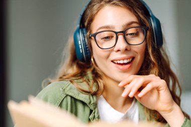 Kablosuz kulaklık takan, rahat bir odada kitap okuyan bir kadının kaybolması. Gözlüklü öğrenci kitap okumayı ve gün ışığında dinlenmeyi sever. Eğitimin kavramsal kavramları, rahatlama, teknoloji.