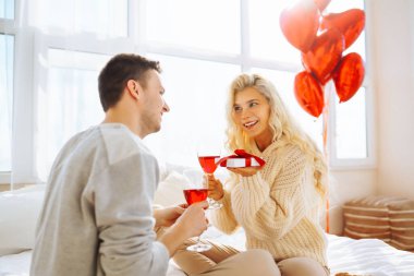 Genç çift, parlak bir odada bir kadeh şarapla birlikte oturur. Erkek, kız arkadaşına balonla süslenmiş bir odada hediyesini sunar. Randevularının tadını çıkarırlar. Tatil ve aşk konsepti. 14 Şubat.