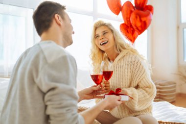 Genç çift, parlak bir odada bir kadeh şarapla birlikte oturur. Erkek, kız arkadaşına balonla süslenmiş bir odada hediyesini sunar. Randevularının tadını çıkarırlar. Tatil ve aşk konsepti. 14 Şubat.