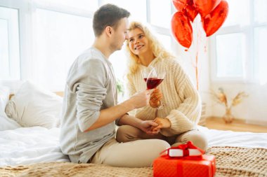 Genç çift, parlak bir odada bir kadeh şarapla birlikte oturur. Erkek, kız arkadaşına balonla süslenmiş bir odada hediyesini sunar. Randevularının tadını çıkarırlar. Tatil ve aşk konsepti. 14 Şubat.