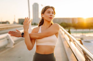 Spor giyimli genç bir kadın güneşli bir köprüde esniyor. Atletik bir kadın sabah sporundan hoşlanır. Konsept: spor, eğlence, aktif yaşam tarzı.