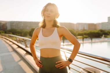 Spor giyimli genç bir kadın güneşli bir köprüde esniyor. Atletik bir kadın sabah sporundan hoşlanır. Konsept: spor, eğlence, aktif yaşam tarzı.
