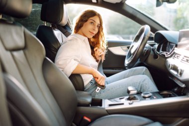 Direksiyondaki genç bir kadın emniyet kemerini bağlıyor. Bir kadın sürücü güvenlik önlemlerini izler ve arabada otururken emniyet kemerini bağlar. Ulaşım ve eğlence kavramı.