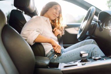 Direksiyondaki genç bir kadın emniyet kemerini bağlıyor. Bir kadın sürücü güvenlik önlemlerini izler ve arabada otururken emniyet kemerini bağlar. Ulaşım ve eğlence kavramı.