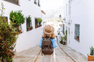 Sırt çantası ve şapkası olan bir turist gün batımında şehrin mimarisine hayran kalır. Güzel bir kadın güneşli bir caddede geziniyor. Turizm, hafta sonları ve tatil kavramları.