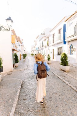 A tourist with a backpack and a hat admires the city's architecture at sunset. A beautiful woman strolls along a sunny street. Concepts of tourism, weekends, and vacations.