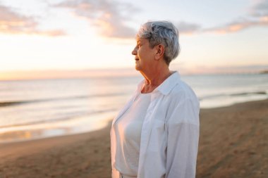 Yaşlı bir kadın gün batımında kumlu bir sahilde yalınayak dolaşır. Gri saçlı bir kadın, deniz kıyısında güneşin doğuşundan zevk alır, özgür hisseder. Emeklilik, özgürlük ve rahatlama kavramları.