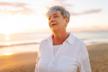 Yaşlı bir kadın gün batımında kumlu bir sahilde yalınayak dolaşır. Gri saçlı bir kadın, deniz kıyısında güneşin doğuşundan zevk alır, özgür hisseder. Emeklilik, özgürlük ve rahatlama kavramları.