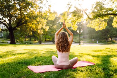 Neşeli bir kadın güneşli bir parkta minder üzerinde yoga yapıyor. Spor elbiseli bir kadın meditasyon yapar, dinlenir ya da zen 'i dışarıda bulur. Meditasyon, rahatlama kavramları.