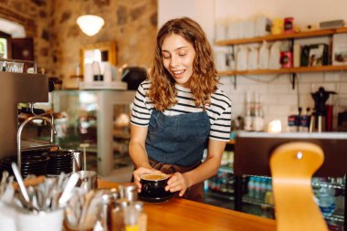 Kadın bir barista tezgahın arkasında duruyor, taze demlenmiş kahve servis ediyor. Önlüklü mutlu bir kadın sıcak bir kahve dükkanında aromatik kahve hazırlar. Küçük işletme konsepti, içkiler.