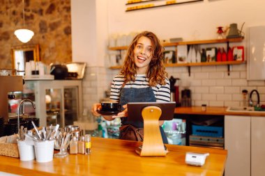Kadın bir barista tezgahın arkasında duruyor, taze demlenmiş kahve servis ediyor. Önlüklü mutlu bir kadın sıcak bir kahve dükkanında aromatik kahve hazırlar. Küçük işletme konsepti, içkiler.