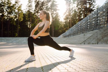 Spor kıyafetli genç bir kadın dışarıda idman yapıyor. Atletik bir kadın gün batımında özel bir platformda ısınır ya da egzersiz yapar. Etkin yaşam biçimi.