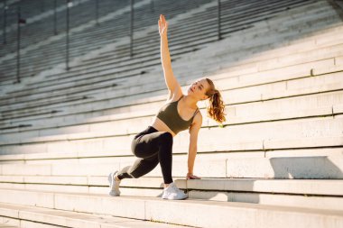 Spor kıyafetli genç bir kadın dışarıda idman yapıyor. Atletik bir kadın gün batımında özel bir platformda ısınır ya da egzersiz yapar. Etkin yaşam biçimi.