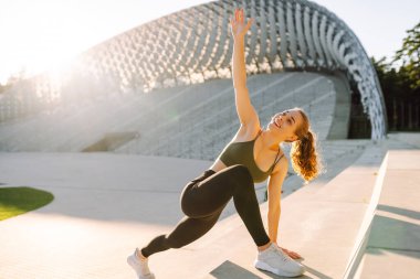 Spor kıyafetli genç bir kadın dışarıda idman yapıyor. Atletik bir kadın gün batımında özel bir platformda ısınır ya da egzersiz yapar. Etkin yaşam biçimi.