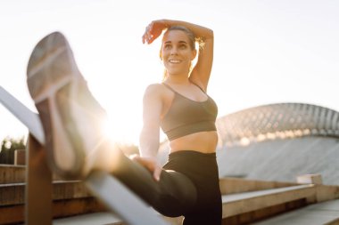 Spor kıyafetli genç bir kadın dışarıda idman yapıyor. Atletik bir kadın gün batımında özel bir platformda ısınır ya da egzersiz yapar. Etkin yaşam biçimi.