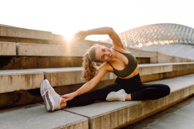 Spor kıyafetli genç bir kadın dışarıda idman yapıyor. Atletik bir kadın gün batımında özel bir platformda ısınır ya da egzersiz yapar. Etkin yaşam biçimi.