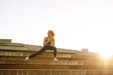 Spor kıyafetli genç bir kadın dışarıda idman yapıyor. Atletik bir kadın gün batımında özel bir platformda ısınır ya da egzersiz yapar. Etkin yaşam biçimi.