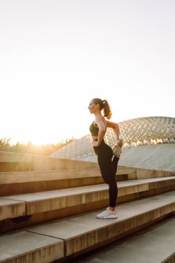 Spor kıyafetli genç bir kadın dışarıda idman yapıyor. Atletik bir kadın gün batımında özel bir platformda ısınır ya da egzersiz yapar. Etkin yaşam biçimi.