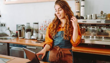 Güneşli bir günde barda elinde dijital tabletle bir kafede duran genç bir kadının portresi. Sıcak bir kahve dükkanında çalışan bayan bir barista. Küçük iş konsepti, içecekler ve teknoloji.