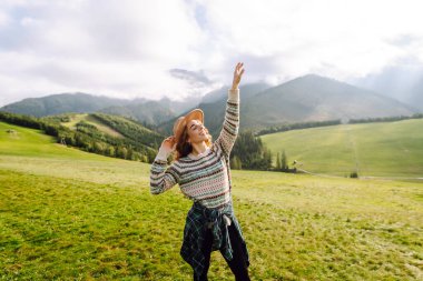 Şapkalı mutlu kadın gün batımında yeşil tepelerin tadını çıkarıyor, özgür hissediyor. Sırt çantalı bir kadın dağlarda yürüyüş parkurunda yürüyor, manzarayı seyrediyor. Özgürlük, rahatlama ve doğa kavramları..