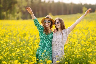 Elbiseli mutlu kız arkadaşlar güneş ışınlarındaki sarı bir tarlada eğleniyorlar. İki genç kadın geziniyor, dışarıda birlikte vakit geçiriyorlar. Arkadaşlık ve moda kavramları.