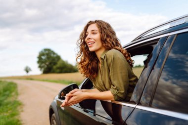 Güzel bir kadın araba camından sarkmış güneşli bir günün tadını çıkarıyor. Genç gezgin açık havanın özgürlüğünü hissediyor. Boş zaman ve ulaşım kavramı.