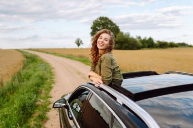 Güzel bir kadın araba camından sarkmış güneşli bir günün tadını çıkarıyor. Genç gezgin açık havanın özgürlüğünü hissediyor. Boş zaman ve ulaşım kavramı.