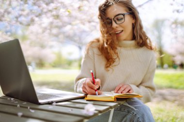 Sunny Park 'taki masada otururken, gözlüklü gülümseyen kadın günlüğüne yazıyor. Güzel bir kadın sarı defteriyle çiçek açan bahçeden hoşlanır. Güzellik kavramları, rahatlama.