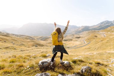 Sarı sırt çantalı mutlu bir yürüyüşçü yürüyüş parkurunda dağ manzarasının tadını çıkarıyor. Genç kadın açık havanın özgürlüğünü hissediyor. Yürüyüş, özgürlük ve macera kavramı.
