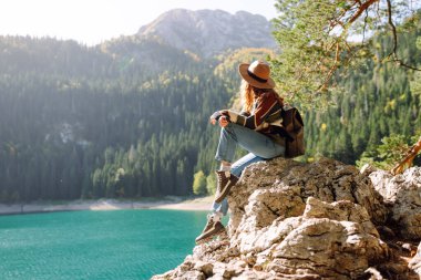 Sarı sırt çantalı mutlu bir yürüyüşçü yürüyüş parkurunda dağ manzarasının tadını çıkarıyor. Genç kadın açık havanın özgürlüğünü hissediyor. Yürüyüş, özgürlük ve macera kavramı.
