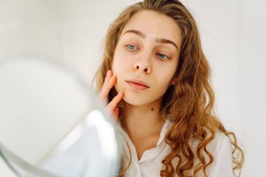 Güneşli bir odada küçük bir aynası olan genç bir kadının portresi. Güzel bir kadın sıcacık bir yerde yansımasına hayran olur. Kavram: güzellik, kozmetoloji.