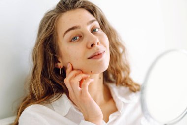 Güneşli bir odada küçük bir aynası olan genç bir kadının portresi. Güzel bir kadın sıcacık bir yerde yansımasına hayran olur. Kavram: güzellik, kozmetoloji.