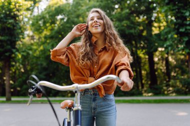 Güneşli bir parkta bisiklet süren genç bir kadın. Neşeli bir turist dışarıda bisiklet sürüyor, doğanın tadını çıkarıyor. Konsept: ulaşım, boş zaman, aktif yaşam tarzı.