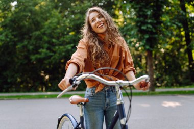 Güneşli bir parkta bisiklet süren genç bir kadın. Neşeli bir turist dışarıda bisiklet sürüyor, doğanın tadını çıkarıyor. Konsept: ulaşım, boş zaman, aktif yaşam tarzı.
