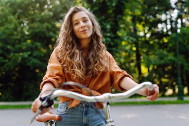 Güneşli bir parkta bisiklet süren genç bir kadın. Neşeli bir turist dışarıda bisiklet sürüyor, doğanın tadını çıkarıyor. Konsept: ulaşım, boş zaman, aktif yaşam tarzı.
