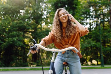 Güneşli bir parkta bisiklet süren genç bir kadın. Neşeli bir turist dışarıda bisiklet sürüyor, doğanın tadını çıkarıyor. Konsept: ulaşım, boş zaman, aktif yaşam tarzı.