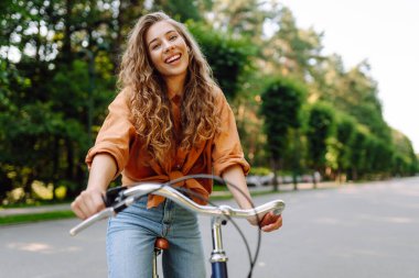 Güneşli bir parkta bisiklet süren genç bir kadın. Neşeli bir turist dışarıda bisiklet sürüyor, doğanın tadını çıkarıyor. Konsept: ulaşım, boş zaman, aktif yaşam tarzı.