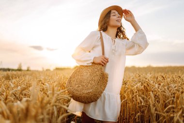 Şapkalı tatlı bir kadın gün batımında buğday tarlasında duruyor. Güzel bir kadın gün batımından zevk alır ve bir çiftlik arazisinde gezinir. Güzellik kavramı, doğa.
