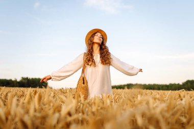 Şapkalı tatlı bir kadın gün batımında buğday tarlasında duruyor. Güzel bir kadın gün batımından zevk alır ve bir çiftlik arazisinde gezinir. Güzellik kavramı, doğa.