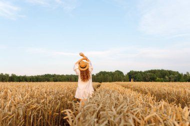 Şapkalı tatlı bir kadın gün batımında buğday tarlasında duruyor. Güzel bir kadın gün batımından zevk alır ve bir çiftlik arazisinde gezinir. Güzellik kavramı, doğa.