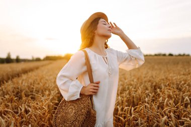 Şapkalı tatlı bir kadın gün batımında buğday tarlasında duruyor. Güzel bir kadın gün batımından zevk alır ve bir çiftlik arazisinde gezinir. Güzellik kavramı, doğa.
